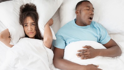 Man in bed suffering from sleep apnea with woman who can't sleep