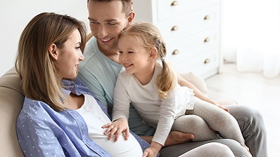 Family on couch with little girl feeling her mother's pregnant belly