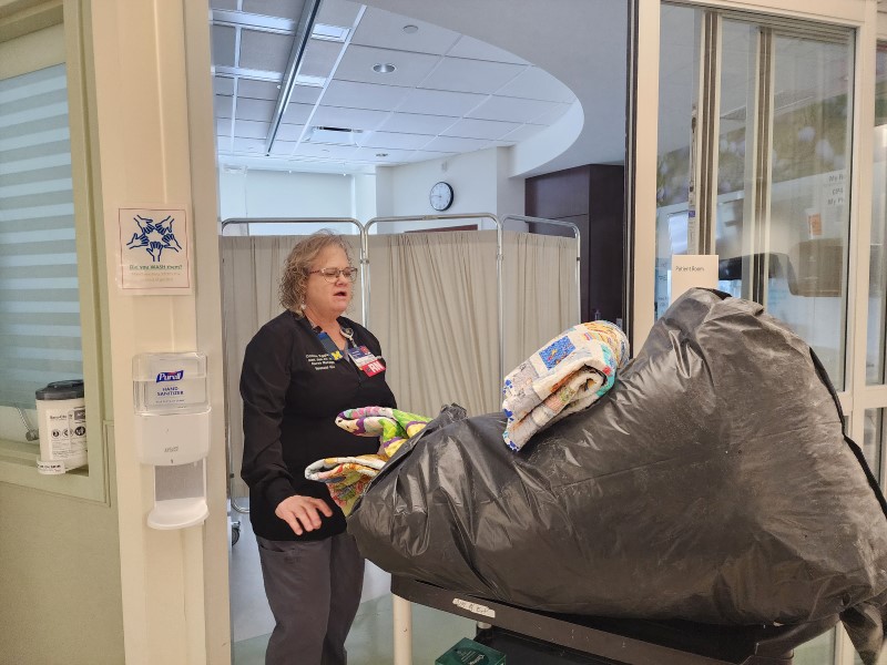 A nurse wheels a large bag of blankets into the NICU