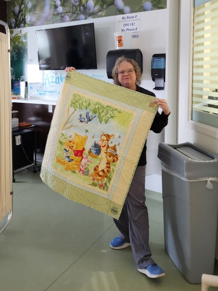 Connie the nurse holds up a Winnie the Pooh quilted blanket