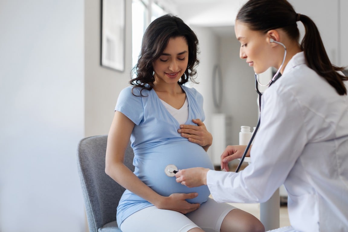 A provider using a stethoscope to examine a pregnant patient 