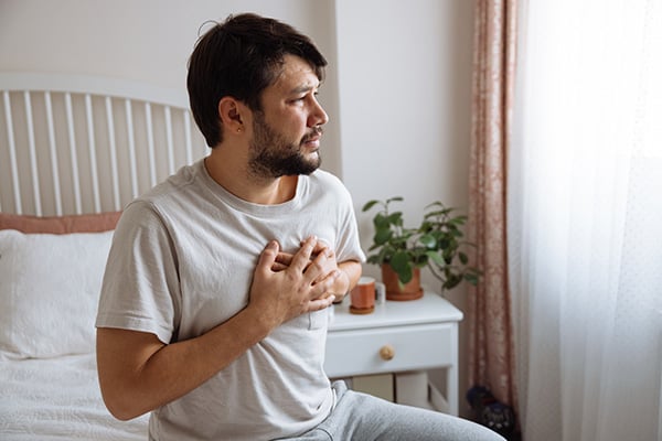Man sitting up in bed holding chest