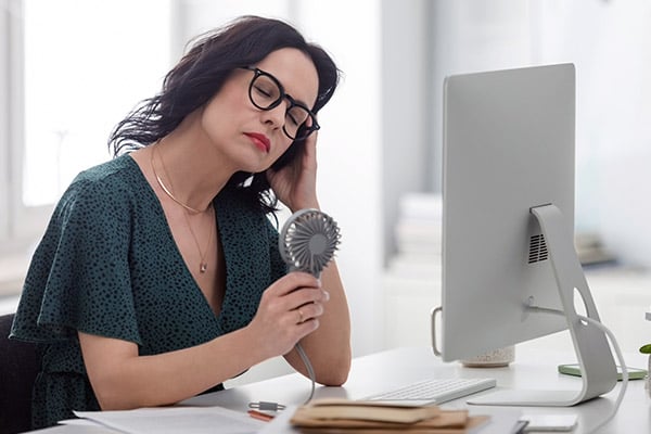 Woman fanning herself while sitting at a desk