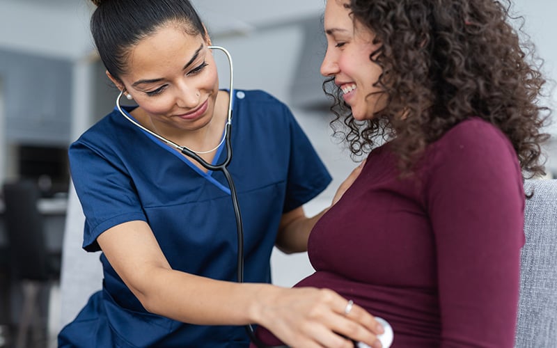 Nurse using stethoscope to examine pregnant woman