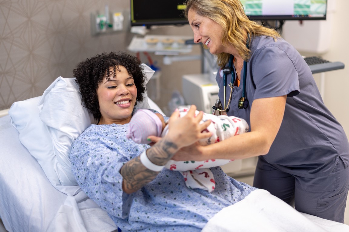 A new mother holding her baby with a caregiver attending