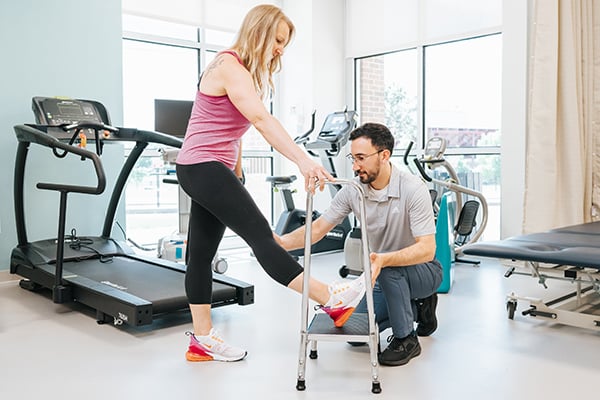 A patient performing a leg stretch while a provider checks for pain