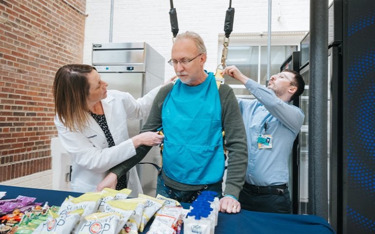 Man receiving help with apron by two individuals