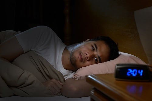 man, laying in bed wide awake, looking at clock